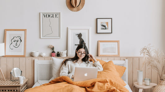 Girl laying in bed in sustainably-styled room reading on laptop