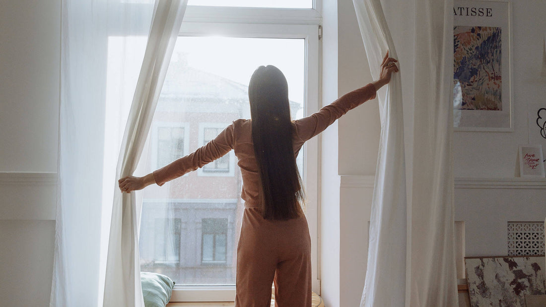 Girl opening curtains at window - Summer Sustainability Tips | HowCork Blog